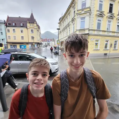 Elijah and Noah grinning with their backpacks on a rainy street
