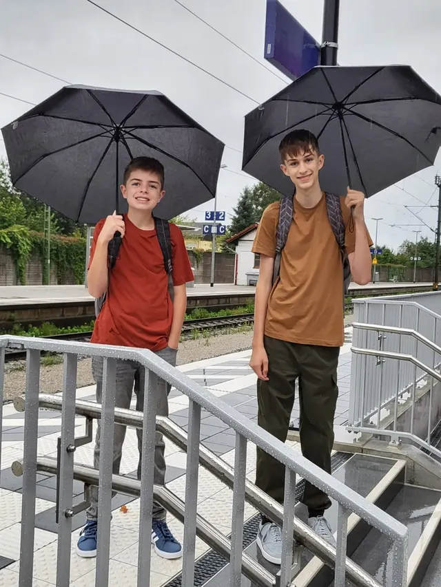 Elijah and Noah smiling under big black umbrellas on a rainy day