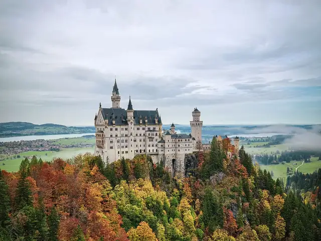 Neuschwanstein Castle above red and orange autumn forest in Schwangau, Bavaria