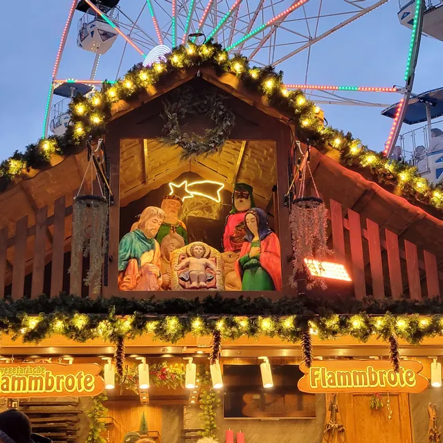 Nativity scene in a wooden hut at the Rosenheim Christmas market, with the Ferris wheel behind