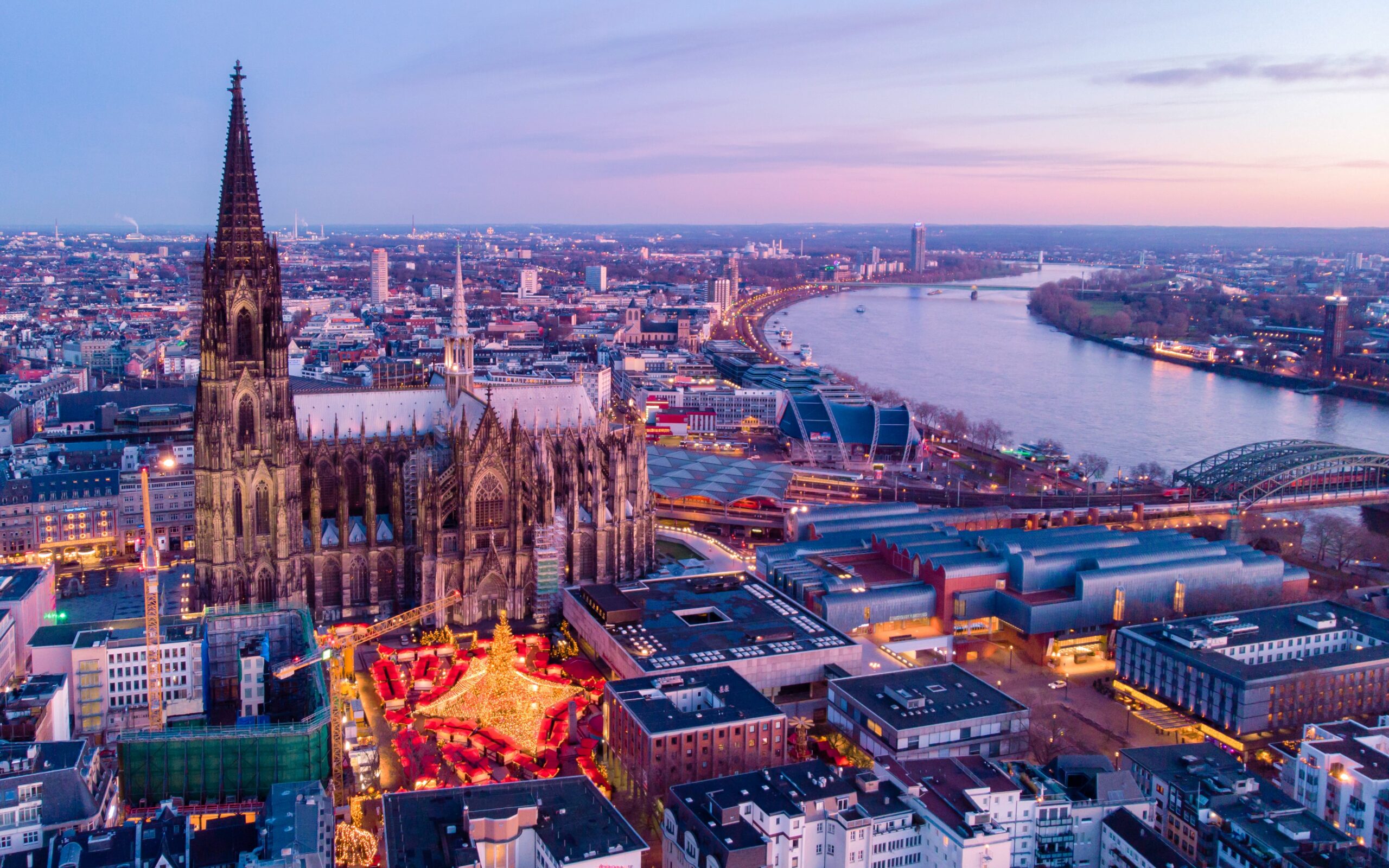Aerial view of a Christmas market lit up at dusk beside Cologne Cathedral, Germany