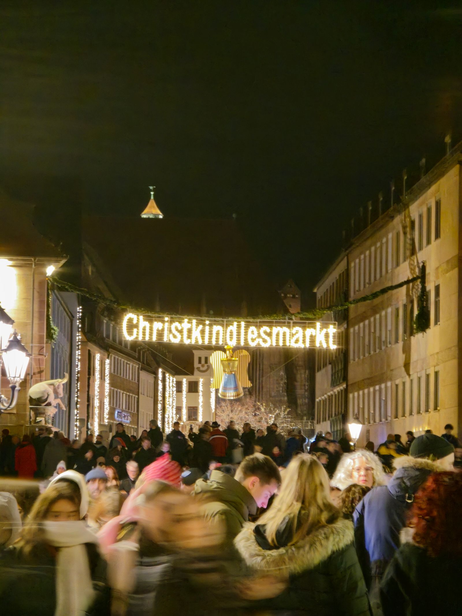 Crowds under the glowing Christkindlesmarkt sign at Nuremberg's Christmas market at night
