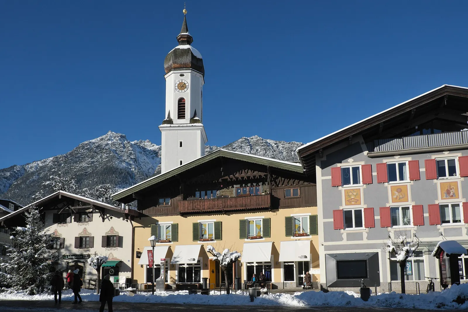Bemalte Häuser und der Turm der Kirche St. Martin in Garmisch-Partenkirchen an einem verschneiten Wintertag